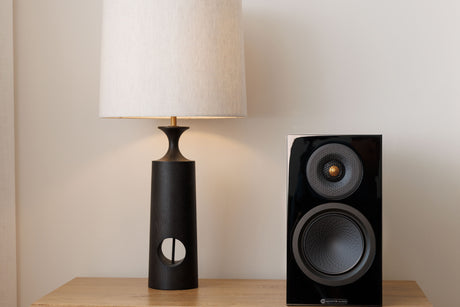 Monitor Audio 8G Silver 50 standmount loudspeaker in black finish sat on a wooden table next to a lamp