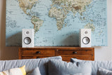 Monitor Audio 8G Silver 50 standmount loudspeaker in white finish sat on a wooden chest of drawers in front of a world map