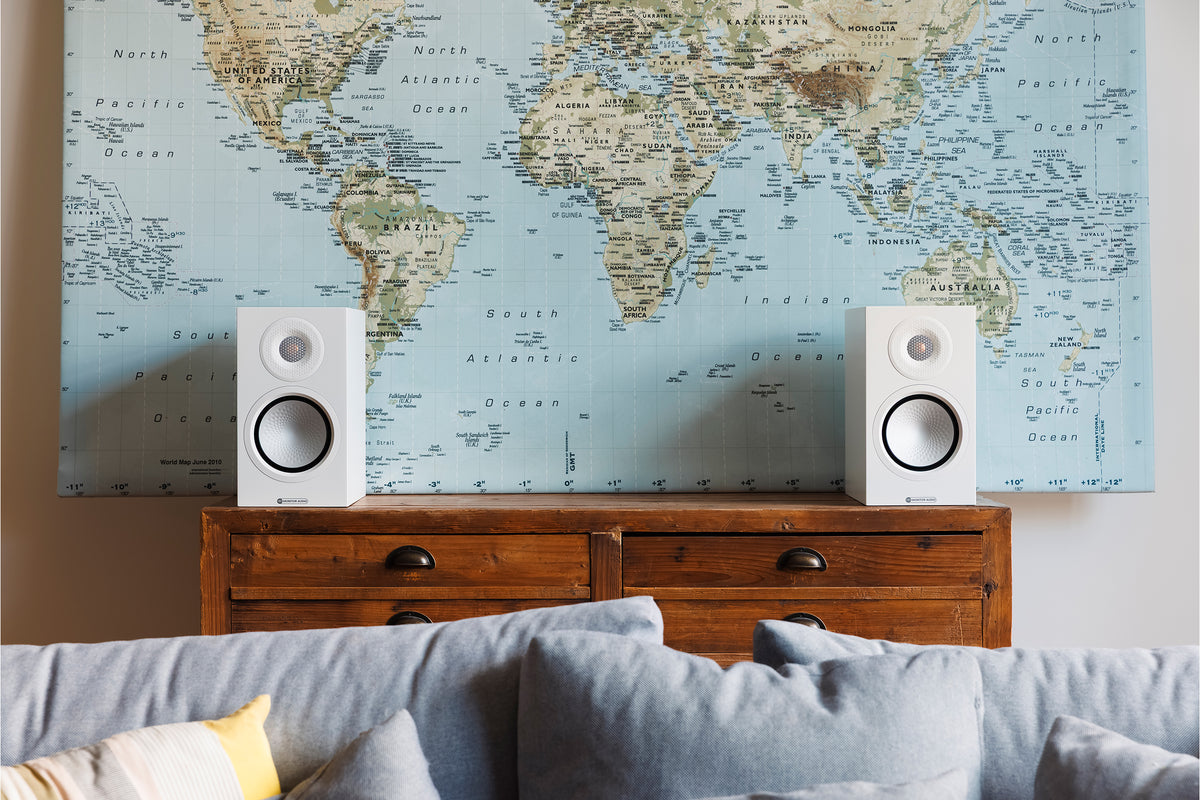 Monitor Audio 8G Silver 50 standmount loudspeaker in white finish sat on a wooden chest of drawers in front of a world map