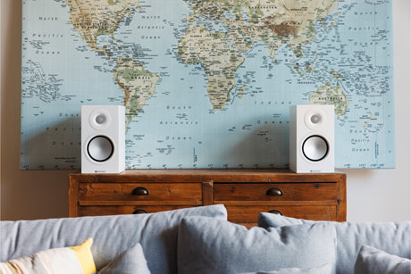 Monitor Audio 8G Silver 50 standmount loudspeaker in white finish sat on a wooden chest of drawers in front of a world map